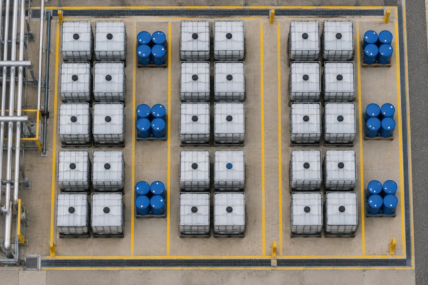 Contentores IBC e tambores alinhados em área de armazenagem com bacia de contenção